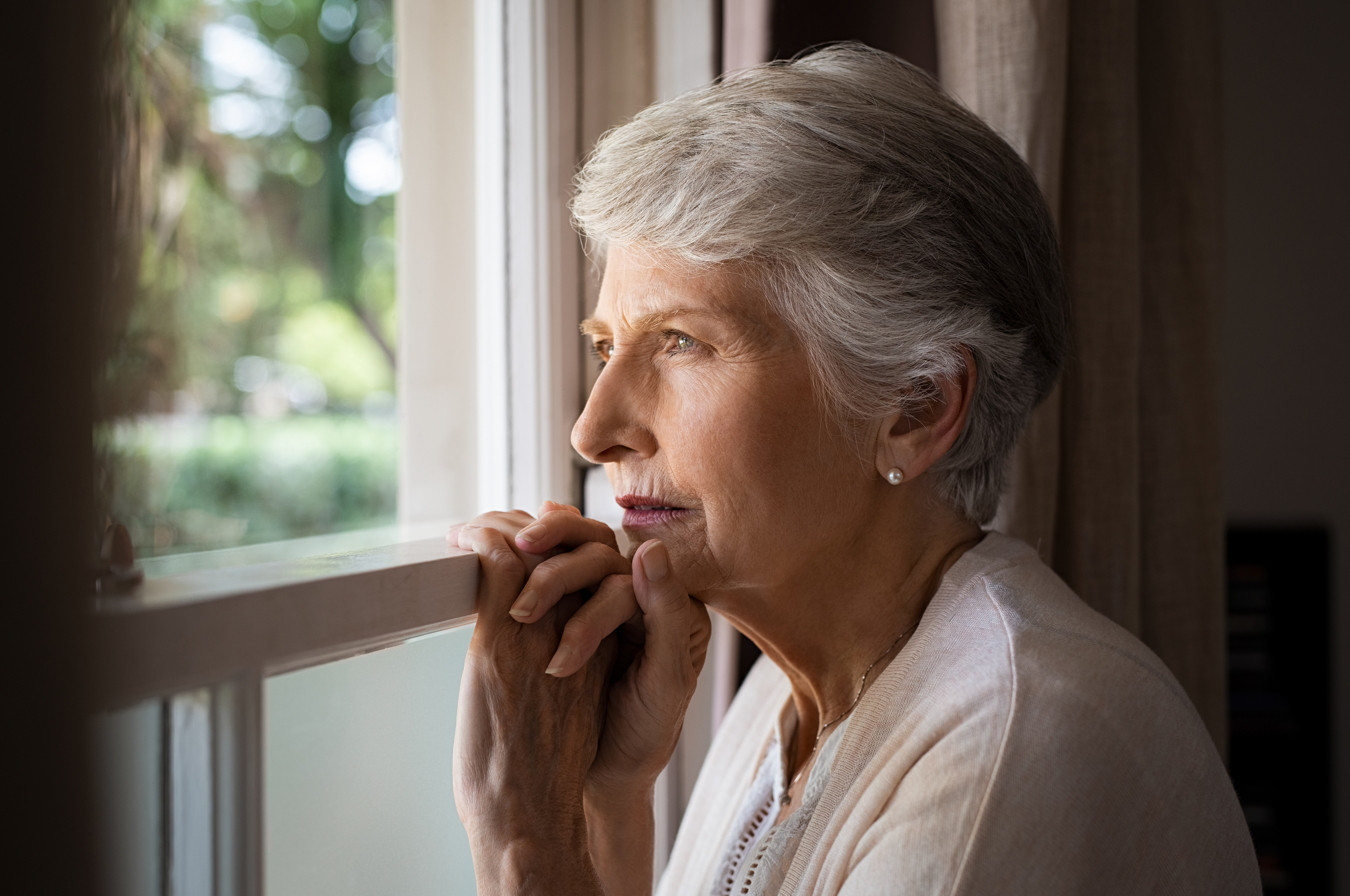 A senior woman, who is experiencing signs of depression, looks out the window.