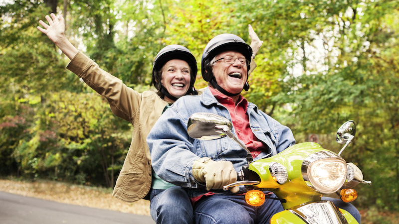A happy senior couple riding a scooter as a way to stay active and healthy this fall